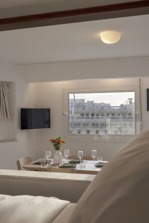 Ein Essbereich mit einem für vier Personen gedeckten Tisch, einem an der Wand montierten Flachbildfernseher und einem Fenster mit Blick auf die Stadt.
