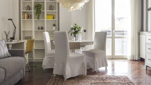 A modern living room with a white sofa, a dining table with chairs, a bookshelf, and a large window. - Casa Margarita, elegant house with parking (Firenze)