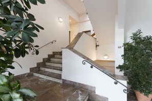 Una escalera con escalones de mármol y barandilla de madera, rodeada de plantas de interior.