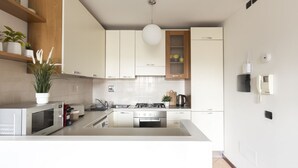 A modern kitchen with white cabinets, a stainless steel stove, a microwave, and a hanging light fixture. - Casa Margarita, elegant house with parking (Firenze)