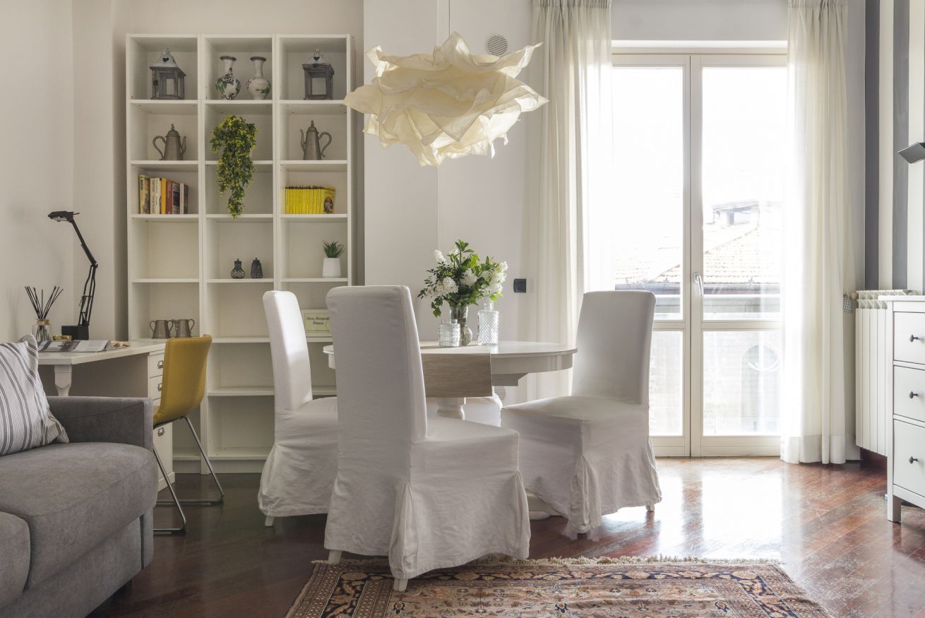 Un soggiorno moderno con un divano bianco, un tavolo da pranzo con sedie, una libreria e un'ampia finestra.