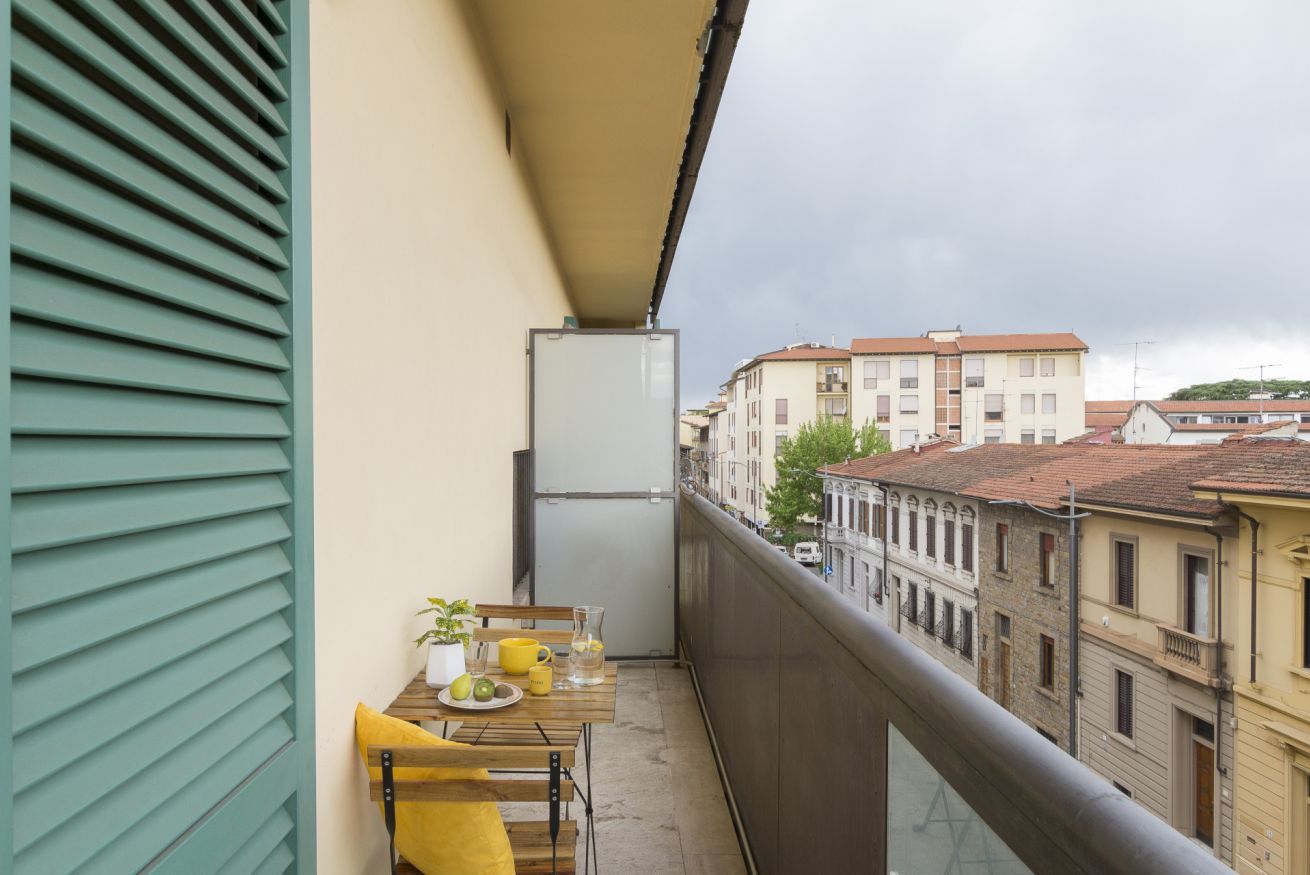 Een balkon met een tafel, stoelen, een koelkast en uitzicht op gebouwen.