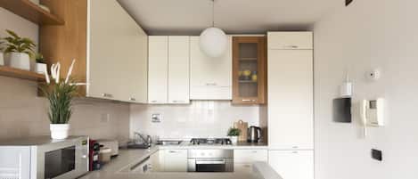 A modern kitchen with white cabinets, a stainless steel stove, a microwave, and a hanging light fixture.