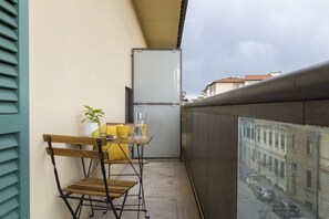 A balcony with a table, chairs, a potted plant, and a refrigerator.