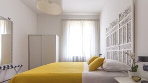 Une chambre d’hôtel comprenant un lit, une armoire, un miroir, une fenêtre avec des rideaux et un panneau décoratif mural.