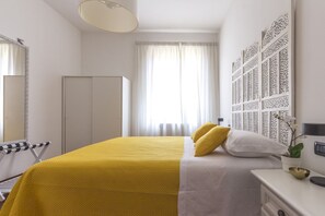 Une chambre d’hôtel comprenant un lit, une armoire, un miroir, une fenêtre avec des rideaux et un panneau décoratif mural.