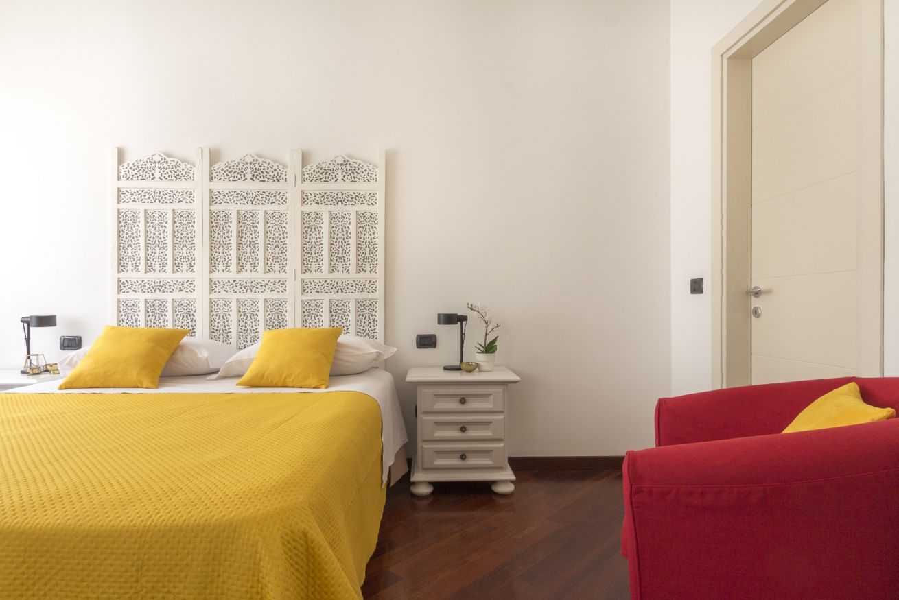 Een hotelkamer met een bed, een nachtkastje, een rode stoel en een witte deur.