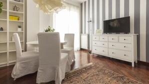 A modern living room with a striped wall, white furniture, a television, and a decorative chandelier. - Casa Margarita, elegant house with parking (Firenze)
