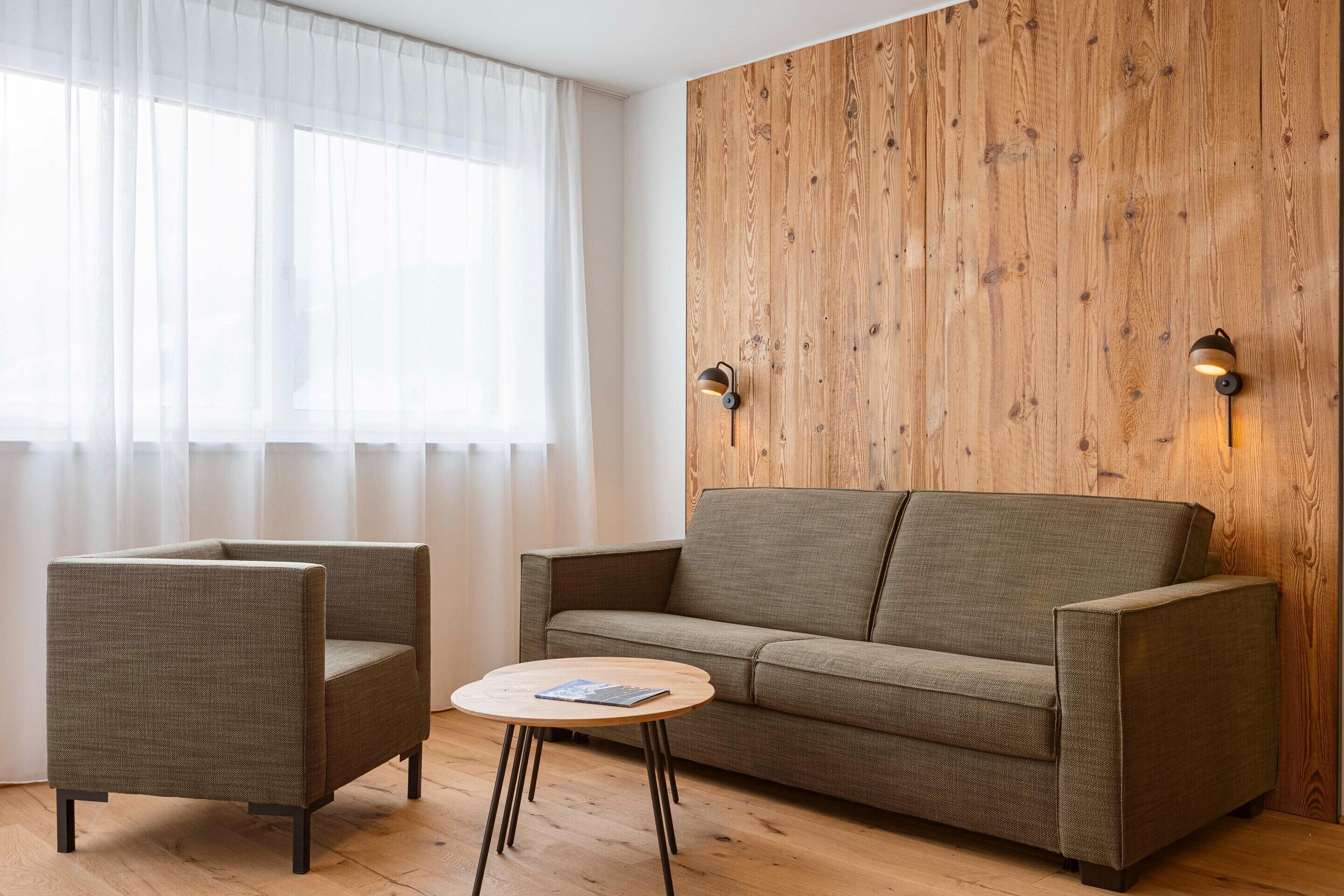 Una sala de estar moderna con una pared de acento de madera, un sofá, dos sillones y una pequeña mesa redonda.