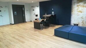 A spacious room with a wooden floor, a blue sofa, a desk with chairs, and a dark blue accent wall. - Kyriad Direct Valence Nord Bourg Les Valence (Bourg-les-Valence)
