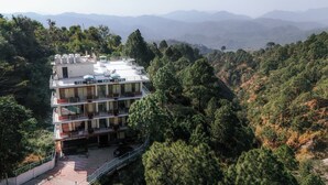 A multi-story hotel with balconies, surrounded by dense forest and mountains in the background. - The White Rain Hotel (Lansdowne)