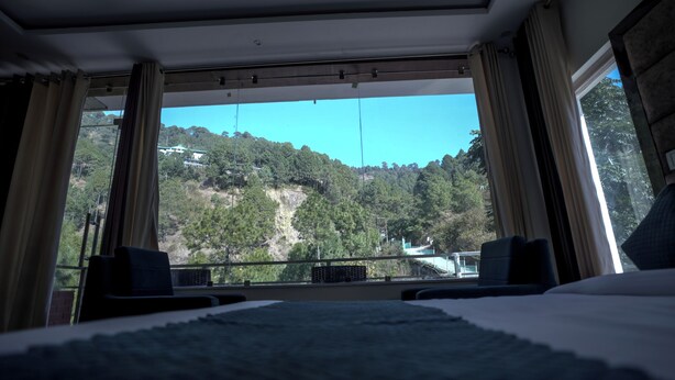 A hotel room with a large bed, a view of a mountainous landscape, and a balcony with a railing. - The White Rain Hotel (Lansdowne)