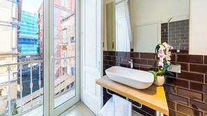 A bathroom with a large window, a white sink, a mirror, and a potted orchid. - Starguest Dante  (Naples)