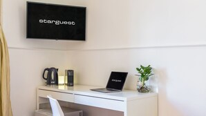 A modern hotel room with a white desk, a laptop, a coffee maker, a plant, and a television displaying "starguest". - Starguest Dante  (Naples)
