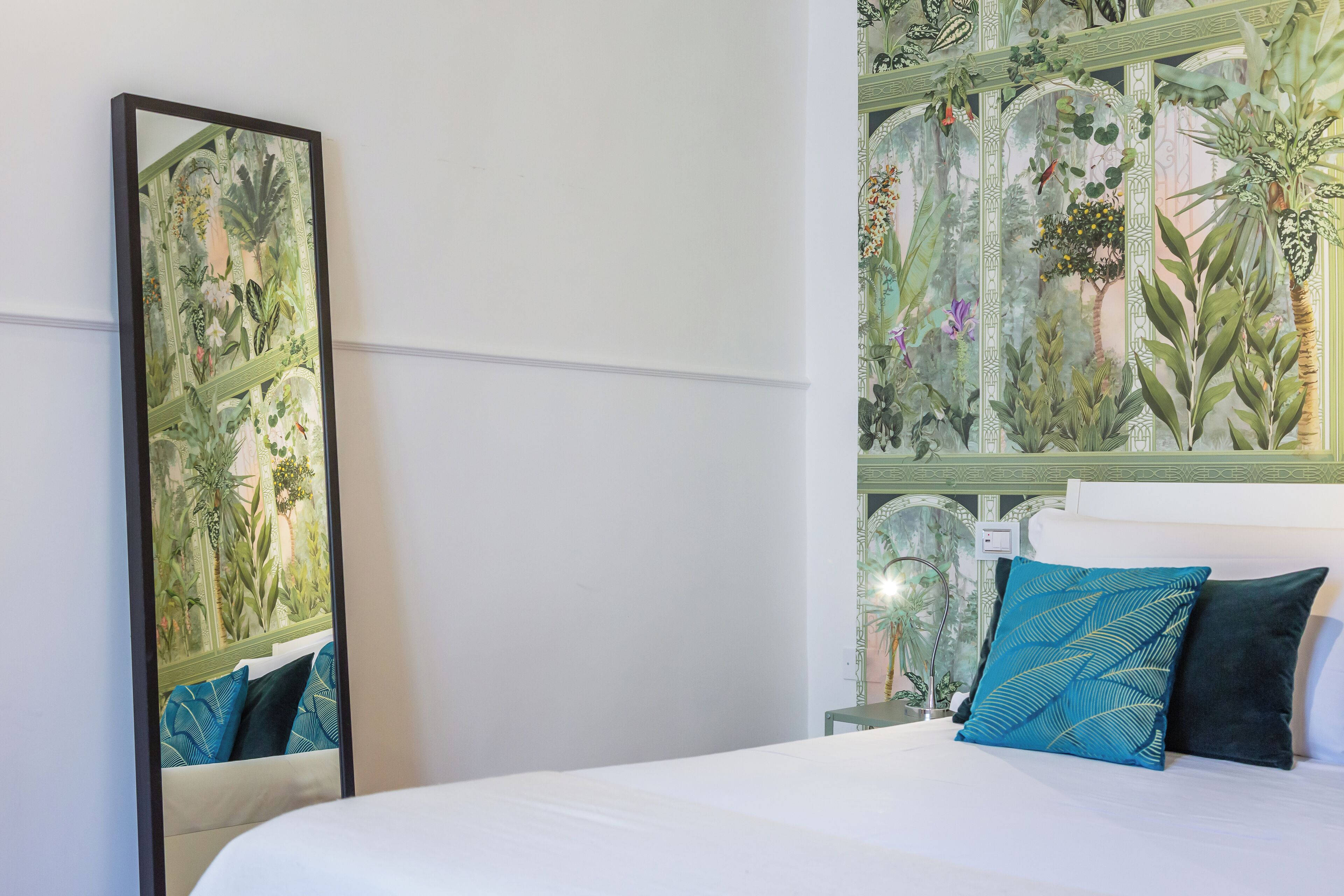 A hotel room with a large mirror, a bed with white bedding, and a decorative wall panel.