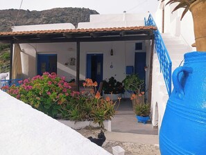 En vit byggnad med en blå dörr, en överbyggd veranda och krukväxter.