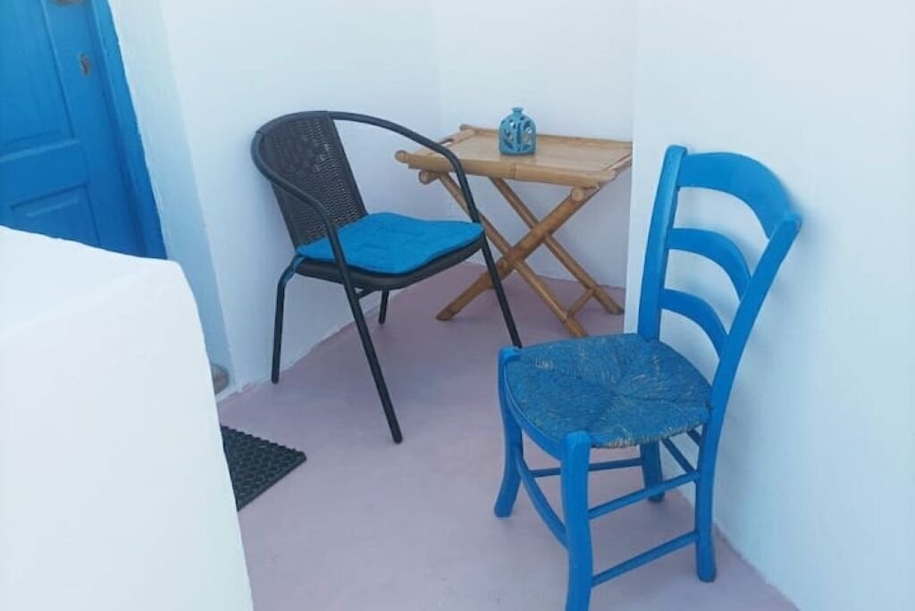 Un piccolo balcone con due sedie, una con seduta intrecciata e l'altra con una seduta blu tinta unita, e un tavolino con un oggetto decorativo sopra.