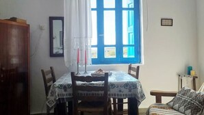 Un coin repas avec une table dressée pour deux personnes, une fenêtre avec des volets bleus et un buffet en bois.