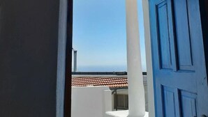 Une vue à travers une porte donnant sur un balcon avec une porte bleue, des murs blancs et un toit recouvert de tuiles.
