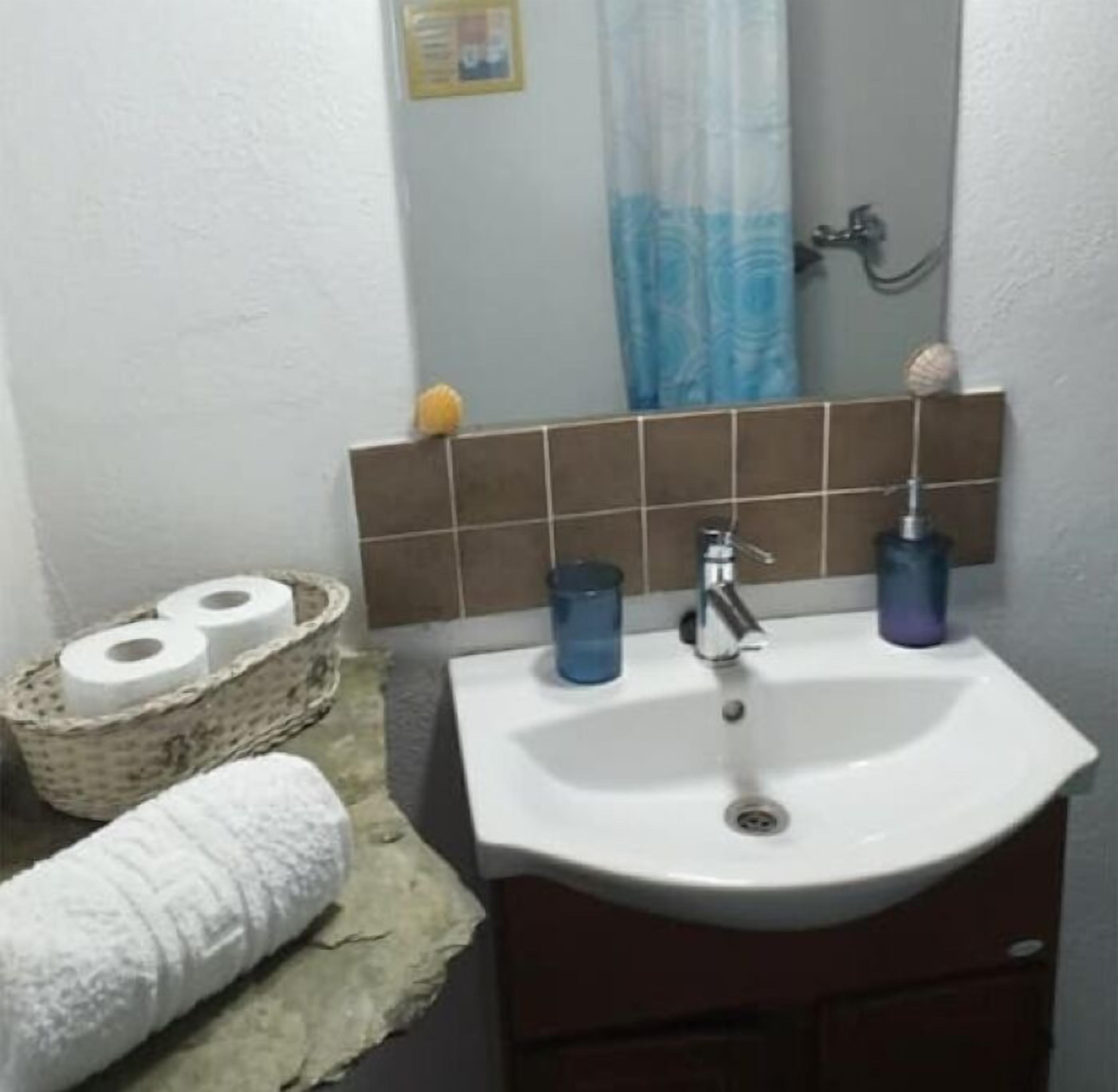 A bathroom with a white sink, two blue soap dispensers, a towel, and a basket of toilet paper.