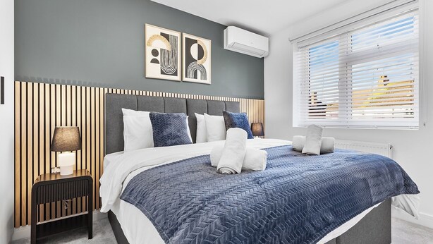 A modern bedroom with a bed, bedside tables, and a window with blinds. - Spacious 4BR Home in Brentford, Free Parking (Brentford)