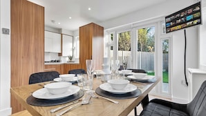 A modern dining area with a wooden table set for four, surrounded by black chairs. - Spacious 4BR Home in Brentford, Free Parking (Brentford)