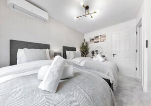 Una habitación de hotel moderna con dos camas, un espejo grande, una planta en maceta y una lámpara en el techo.