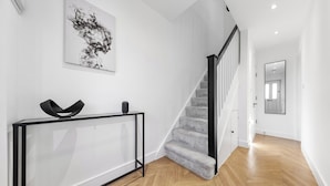A modern interior with a staircase, a console table, and a large abstract painting on the wall. - Spacious 4BR Home in Brentford, Free Parking (Brentford)