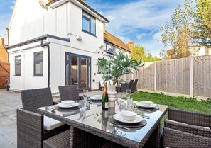 Ein modernes Haus mit einer Terrassenanlage, ausgestattet mit einem Tisch mit Glasplatte, Weidekorbstühlen und einem Blumentopf.