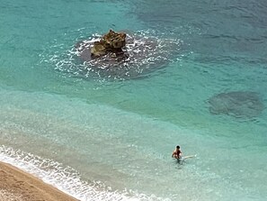 Una playa con agua turquesa cristalina y una persona en el agua.