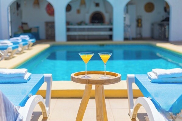 Zona de piscina con sillones de descanso y una mesa con dos copas de martini.