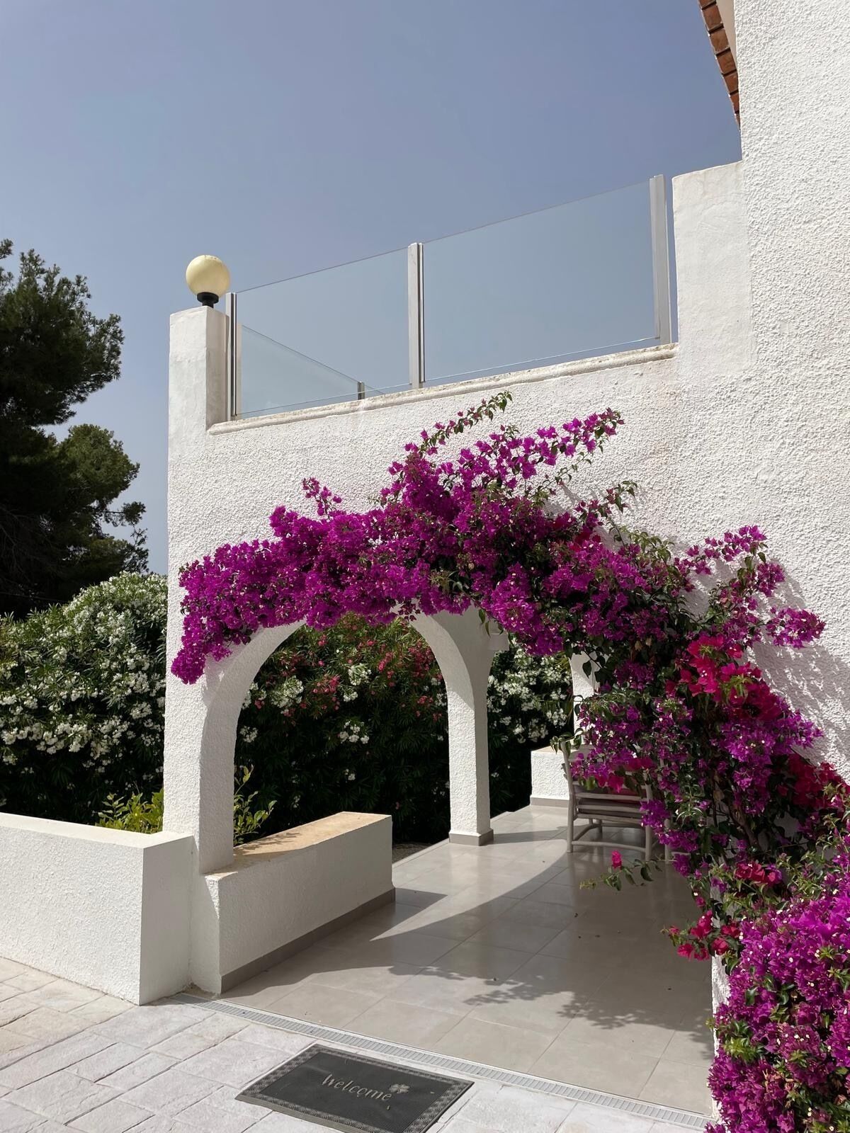Un bâtiment blanc doté d’un balcon et d’une pergola recouverte de fleurs violettes.