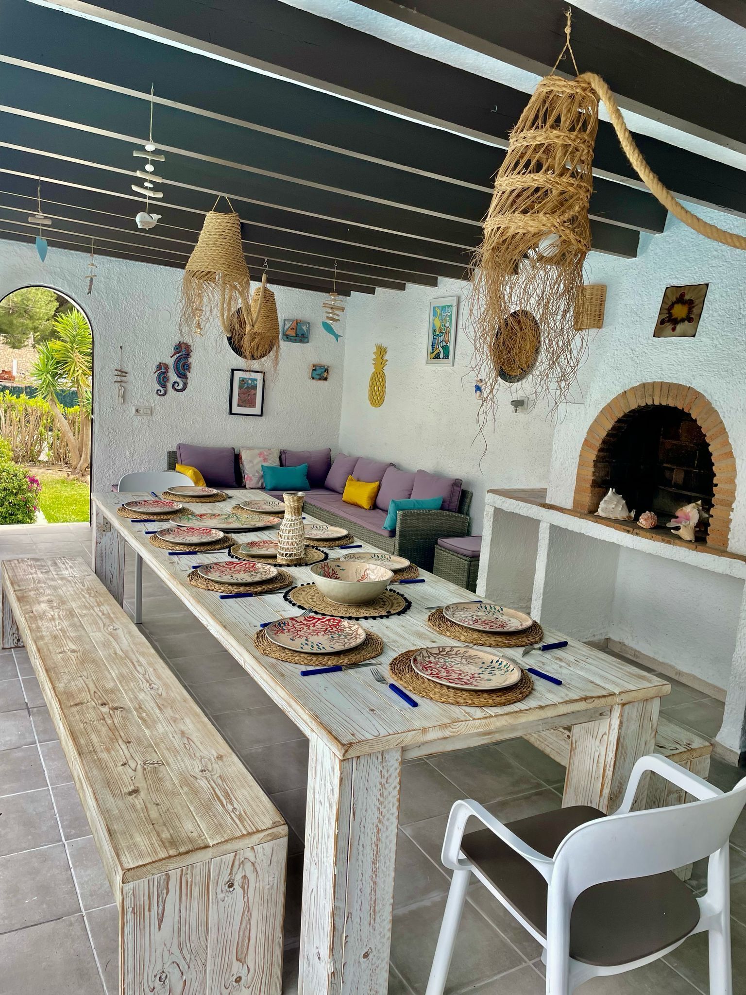 A dining area with a long wooden table set for a meal, a white chair, and a rustic brick fireplace.