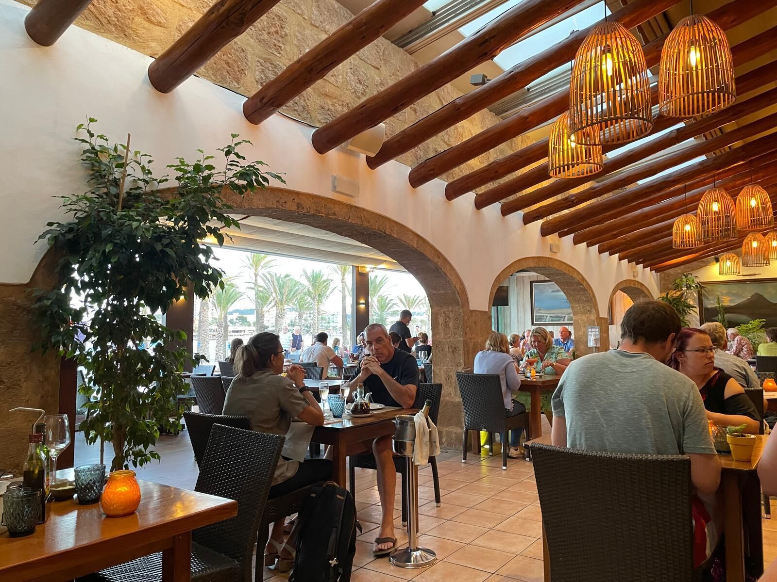 An indoor dining area with wooden beams, tables, chairs, and hanging light fixtures.