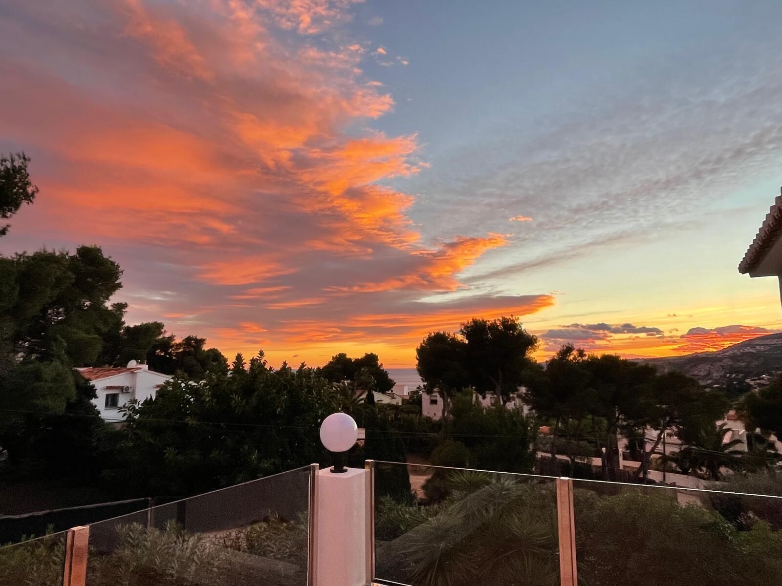 A sunset view from a balcony with a railing and a spherical light fixture.