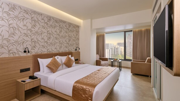 Een moderne hotelkamer met een groot bed, een nachtkastje met een telefoon, een klein tafeltje met een schaal fruit, en een aan de muur bevestigde televisie.