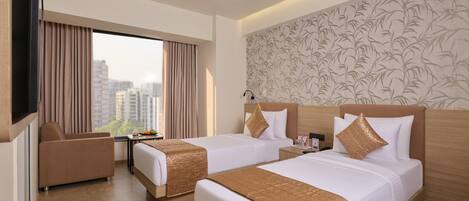 A hotel room with two beds, a TV, a desk, and a view of the city.