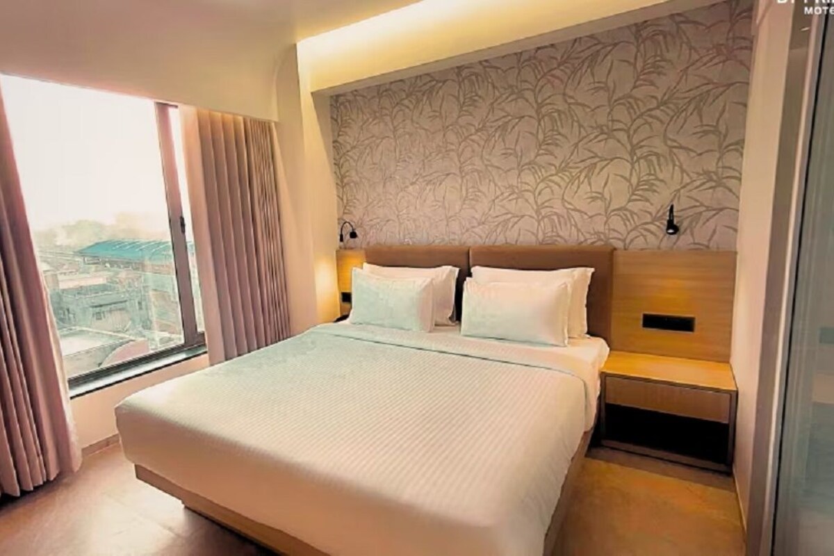 Ein Hotelzimmer mit einem großen Bett, Blick durch das Fenster und einer Wand mit Muster.