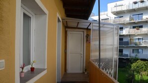 A narrow balcony with a wooden floor, a white door, and a window with potted plants. - Vega - Free Parking - Self Checkin (Graz)