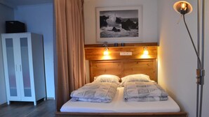 A bedroom with a wooden headboard, two pillows, a bed, a nightstand, a wall-mounted light, and a framed picture above the bed. - Vega - Free Parking - Self Checkin (Graz)