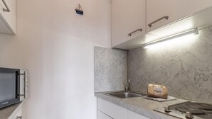 A kitchen with white cabinets, a built-in microwave, a marble backsplash, a stainless steel sink, and a loaf of bread on the counter.