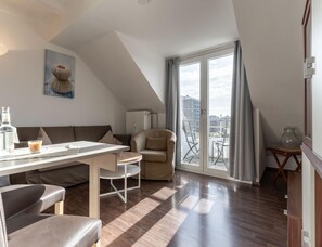 Un salon moderne comprenant un coin repas, un canapé, un fauteuil et une vue sur la ville grâce à de grandes fenêtres.