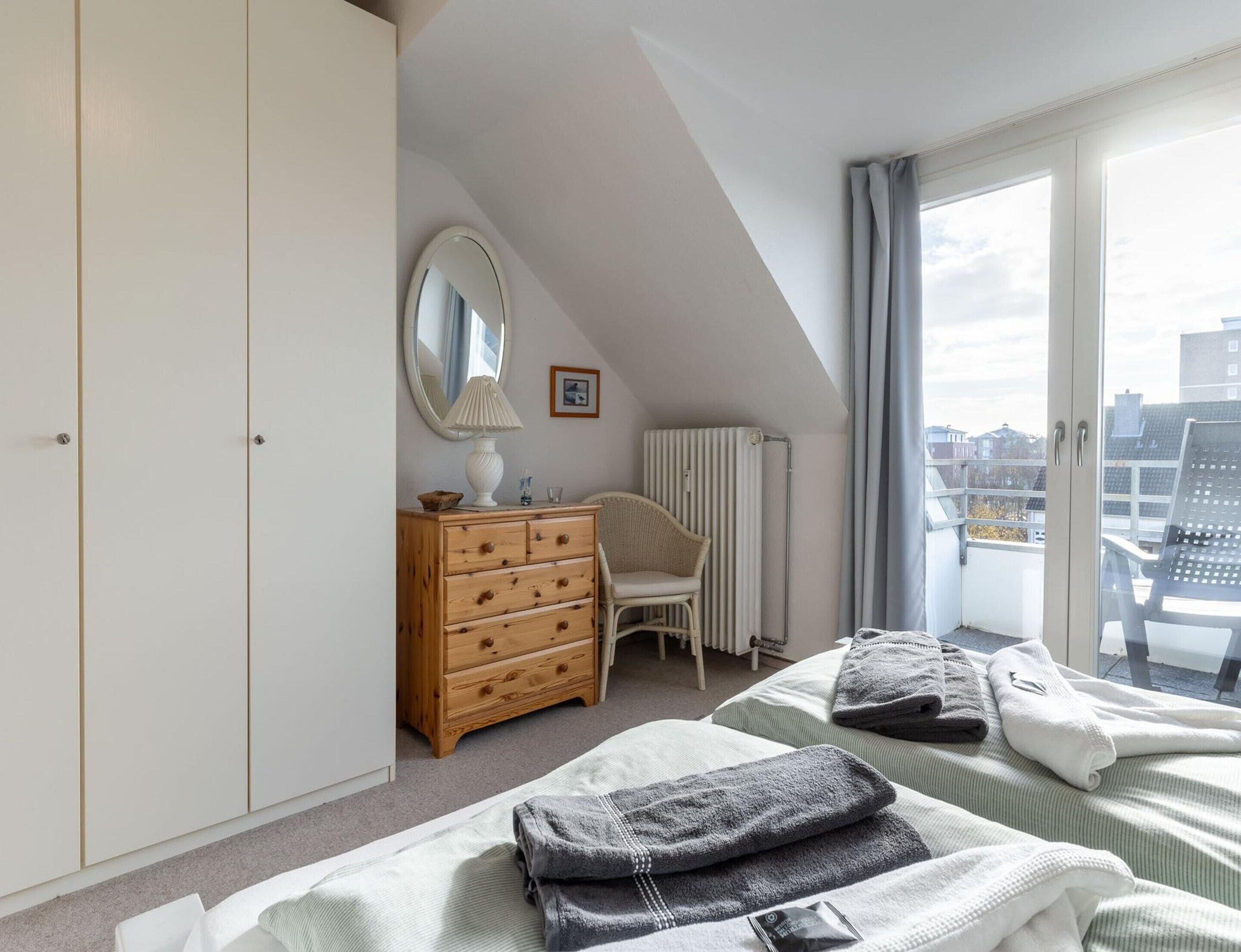A bedroom with a bed, a dresser, a chair, a radiator, and a window with a view of buildings.