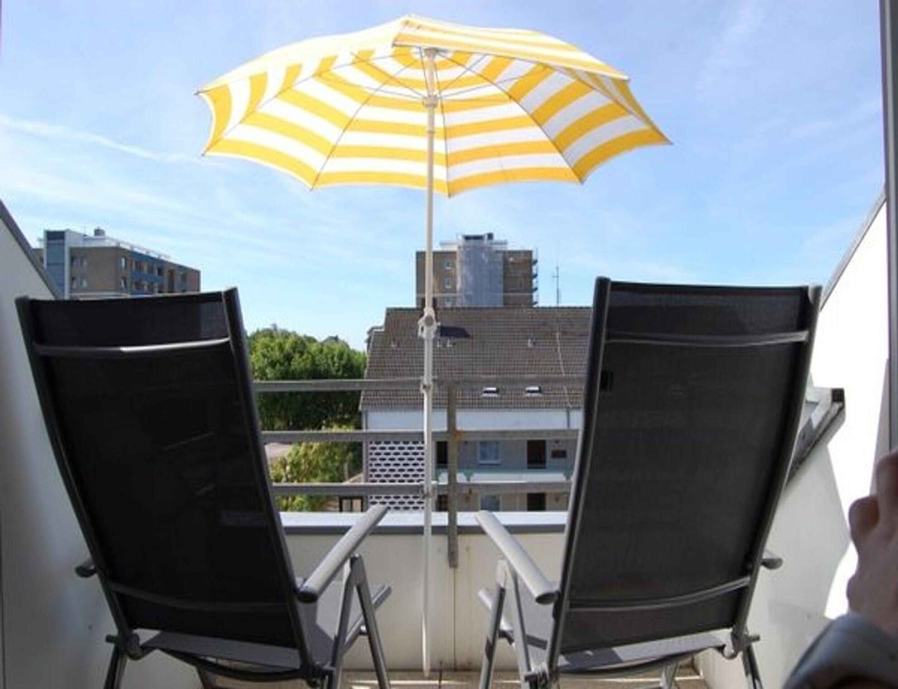 A balcony with two black chairs and a yellow and white striped umbrella.