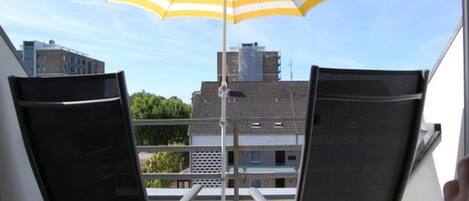 En balkon med to sorte stole og en gul og hvid stribet parasol.