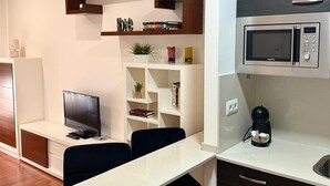 Een moderne keuken met een magnetron, koffiezetapparaat en een eethoek met een televisie en boeken.
