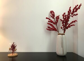 A vase with red branches on a dark surface against a white wall.