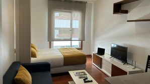 Een moderne hotelkamer met een bed, een bank, een televisie en een raam met jaloezieën.