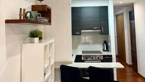Een compacte keuken met moderne apparaten, een eethoek met twee stoelen, en een klein plankje met decoratieve objecten.
