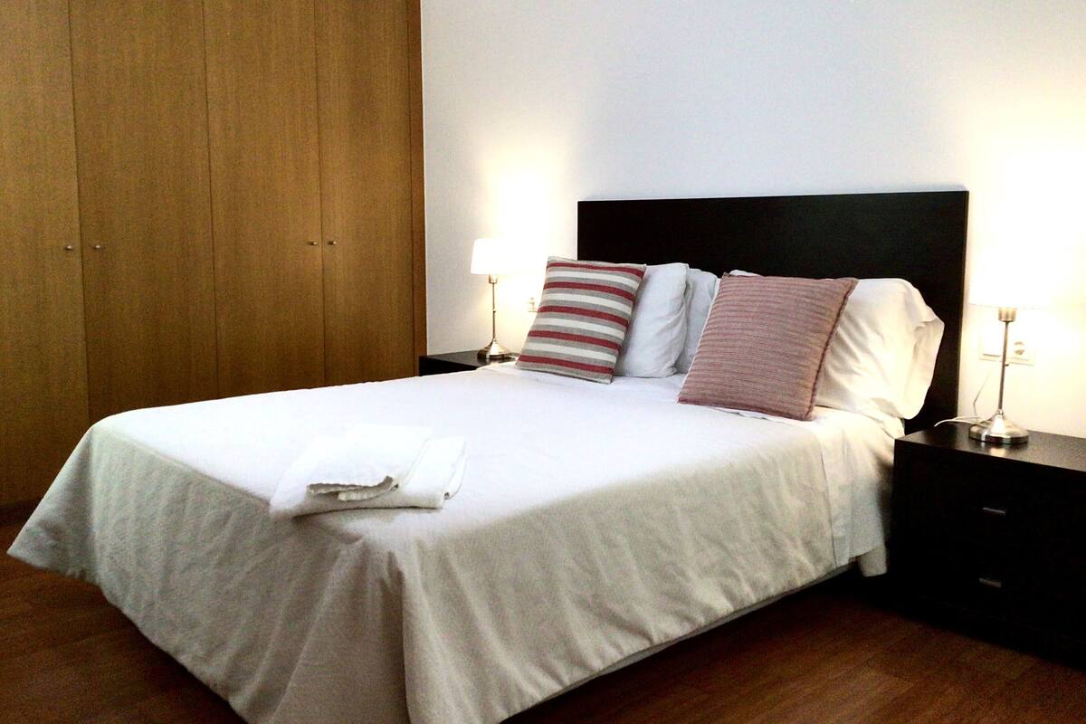 Un lit bien fait, avec des oreillers, une table de chevet avec une lampe et une armoire en bois.